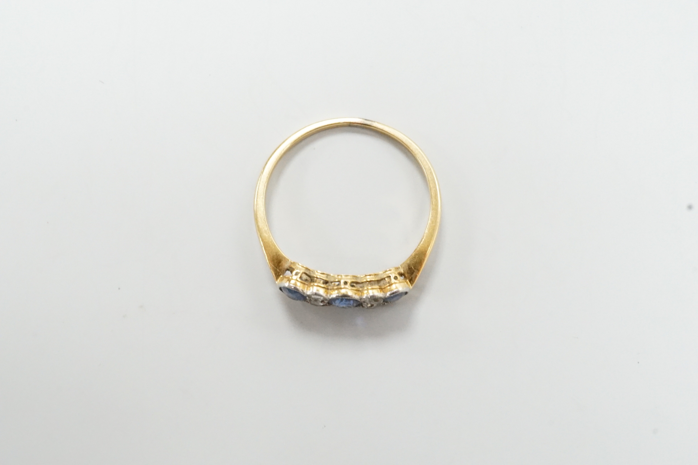 An early 20th century yellow metal and three stone oval cut sapphire set ring, with four stone diamond spacers, size O, gross weight 2 grams.